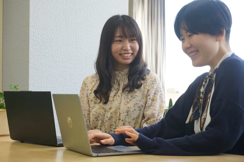 ノートパソコンを前に先輩と話す新入社員